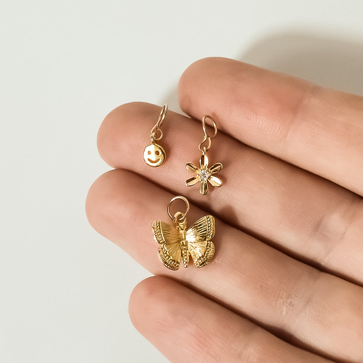 model holding gold charms pendants, butterfly, flower, smiley