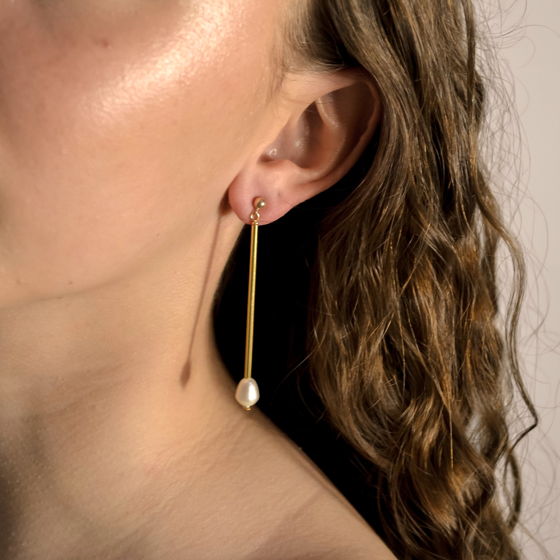 Model wearing Freya long drop gold and pearl earrings 